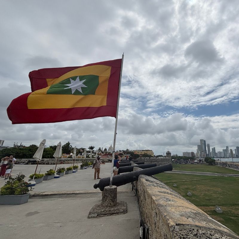 Colombian flag waving beside old fortress cannons overlooking Cartagena’s skyline and waterfront.