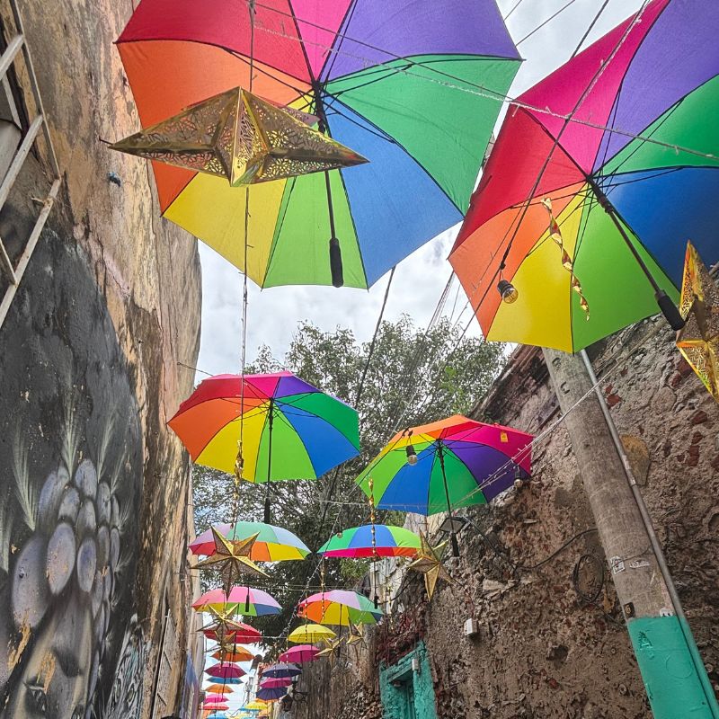 Narrow Cartagena alleyway decorated with colorful hanging umbrellas and star lanterns overhead.