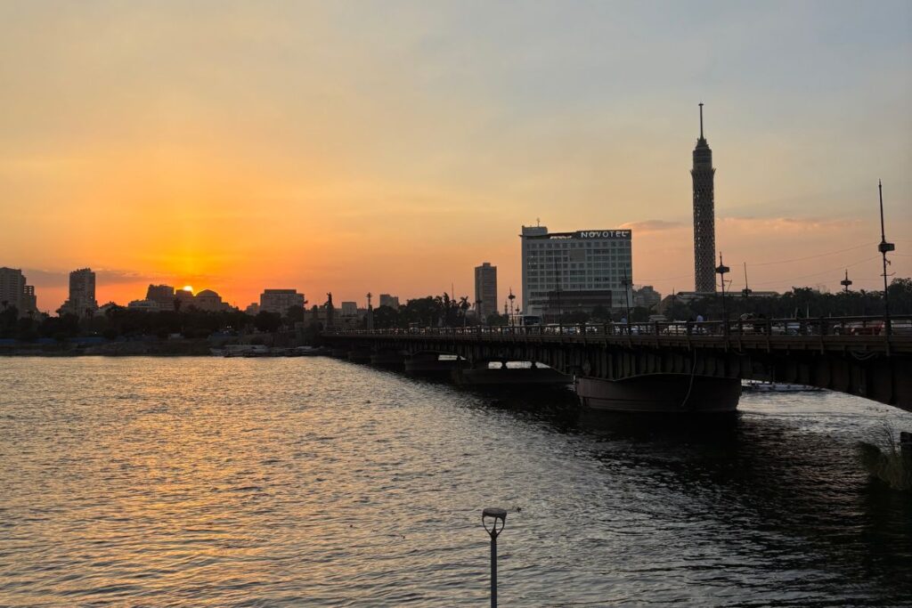 Sunset over the Nile River in Cairo with city skyline, bridge, and Cairo Tower in the background.