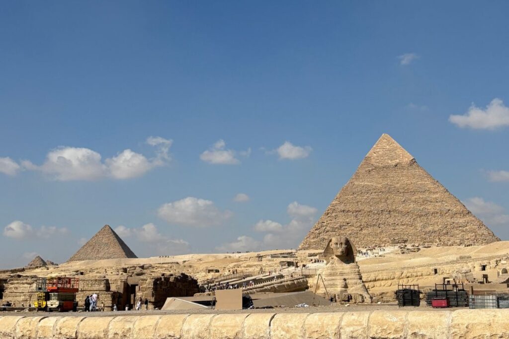 Wide view of the Great Pyramids of Giza and the Sphinx under a bright blue sky in Egypt.