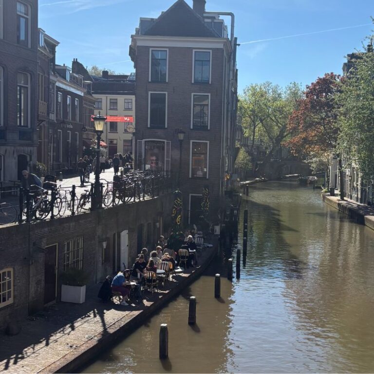 Historic canal lined with cafés, bicycles, and traditional Dutch buildings on a sunny afternoon in Utrecht, Netherlands.