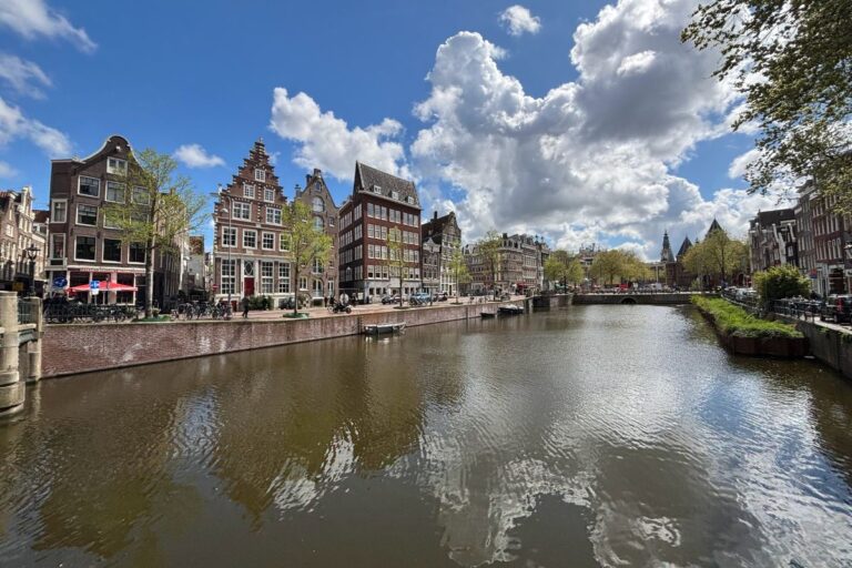 Historic canal houses reflected along a sunny canal in central Amsterdam during spring.