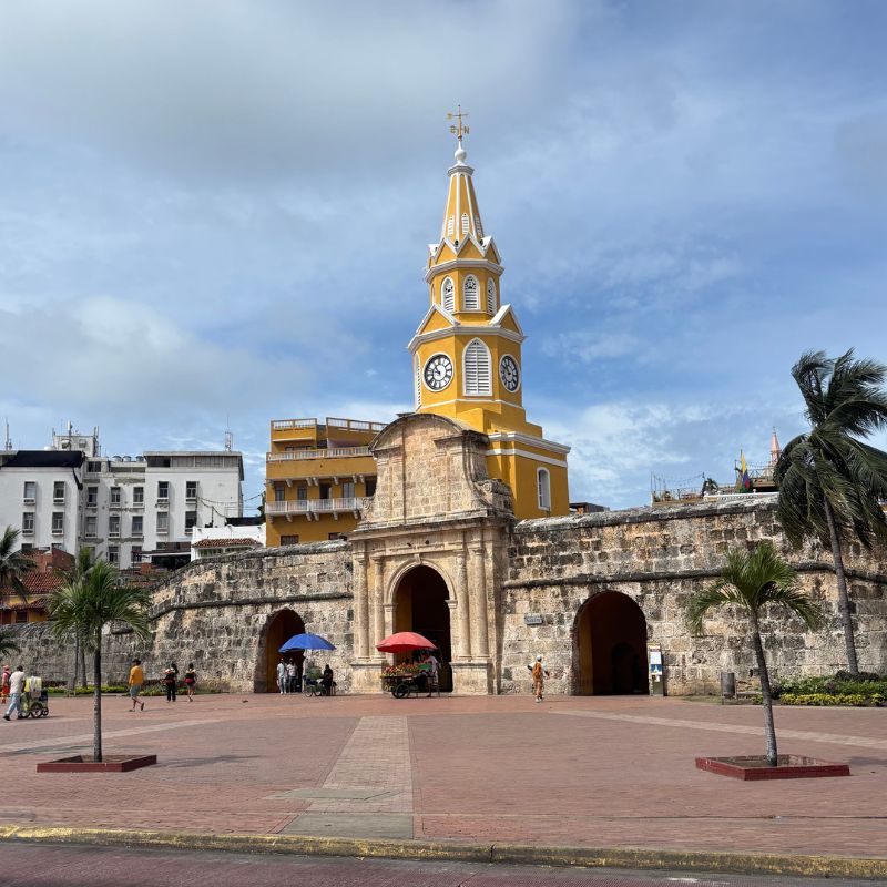 palm trees.
Historic yellow clock tower entrance at Cartagena’s walled city under cloudy skies.
