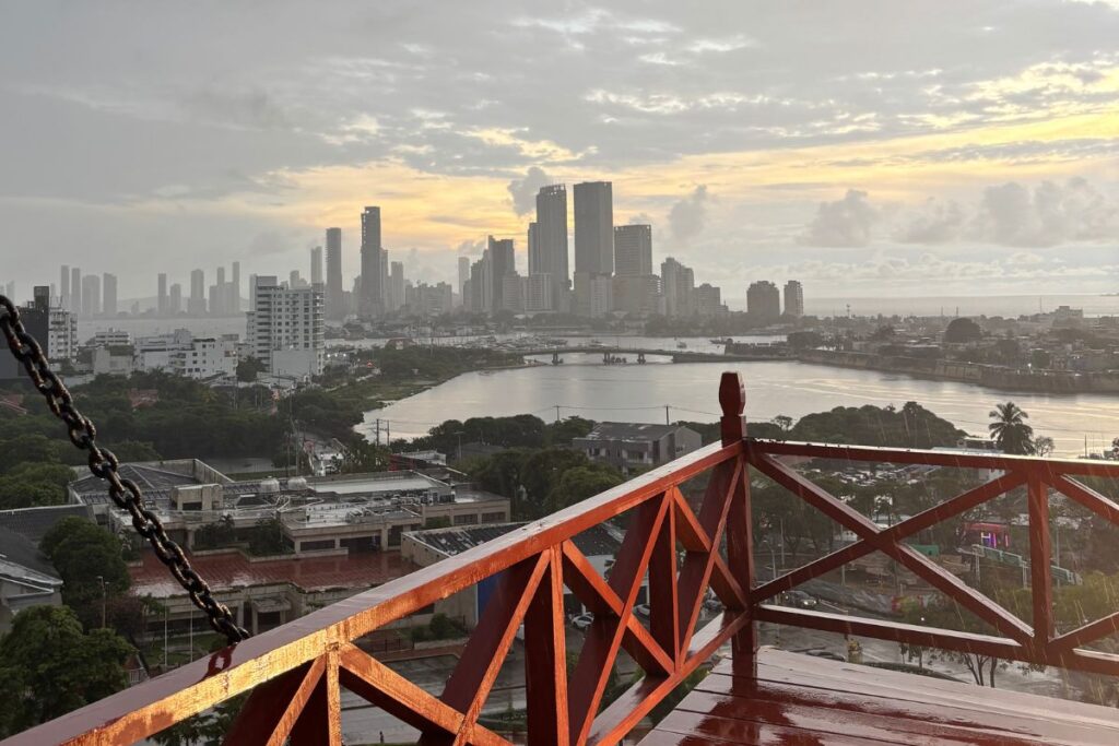 Rainy sunset view over Cartagena’s skyline and waterfront from a terrace with red wooden railings at Castillo San Felipe de Barajas fortress
