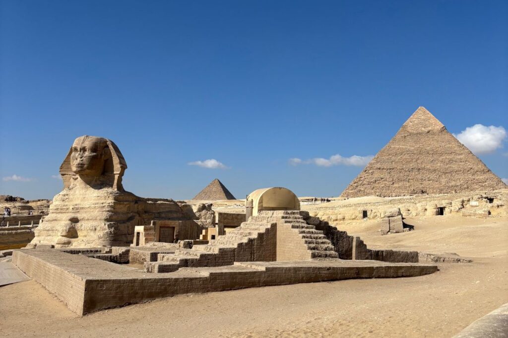Panoramic view of the Great Sphinx with the pyramids of Giza in the background on a sunny afternoon.