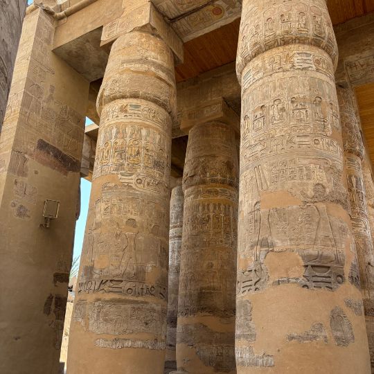 Massive carved stone columns covered in hieroglyphics inside an ancient Egyptian temple courtyard.