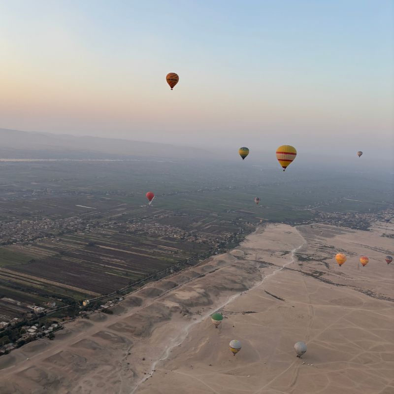 Hot air balloons floating above the desert and green farmland near Luxor at sunrise, viewed from high above the Nile Valley.