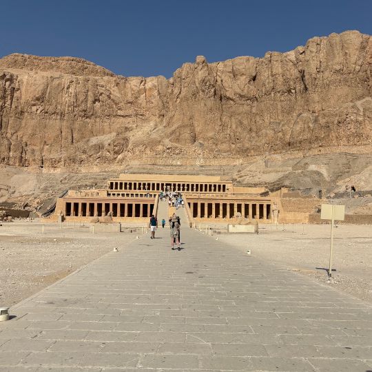Long stone walkway leading toward the Temple of Hatshepsut set against towering desert cliffs in Luxor.
