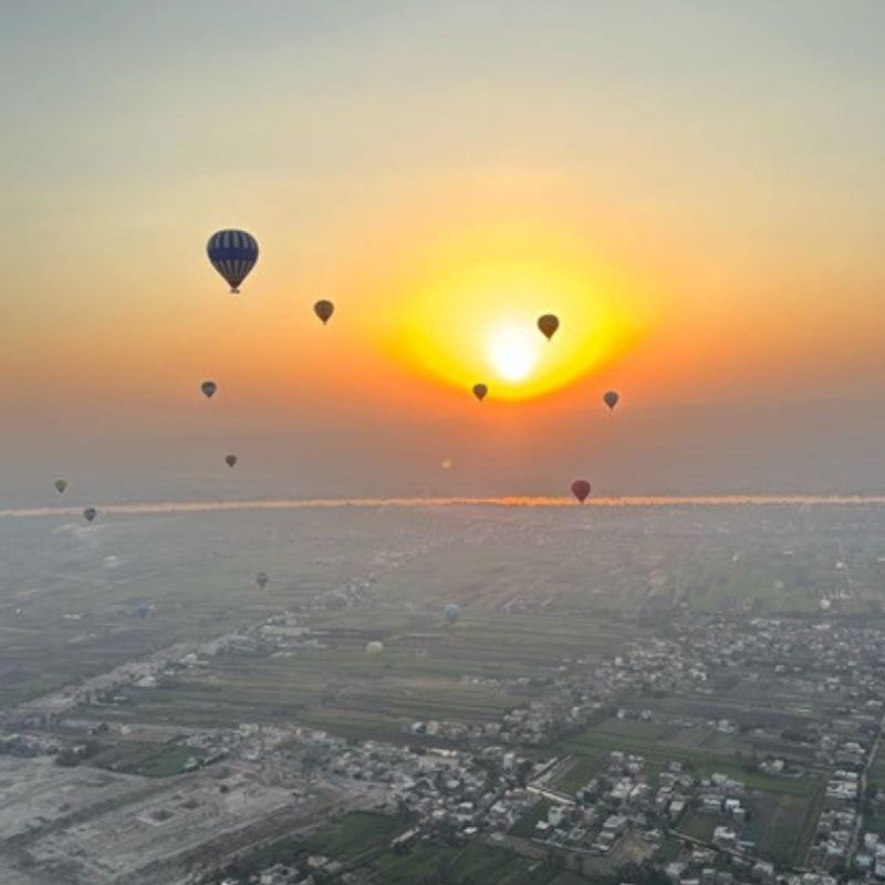 Sunrise hot air balloon flight over Luxor, Egypt, with balloons floating above the Nile Valley.