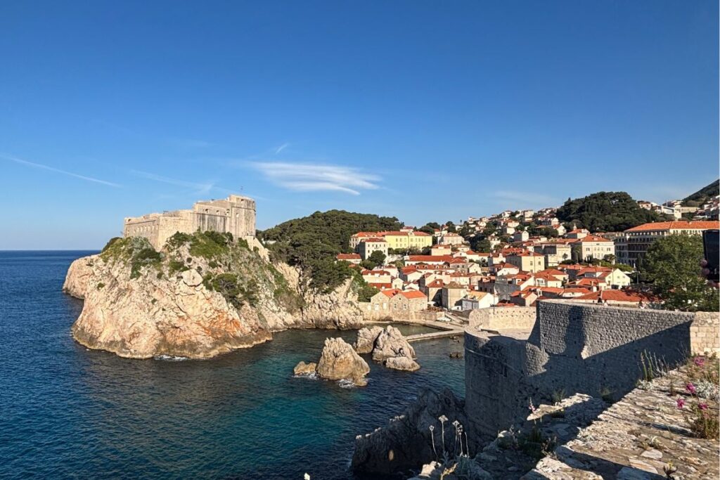 View of Dubrovnik’s stone walls and seaside fortress overlooking the Adriatic Sea on a sunny afternoon.