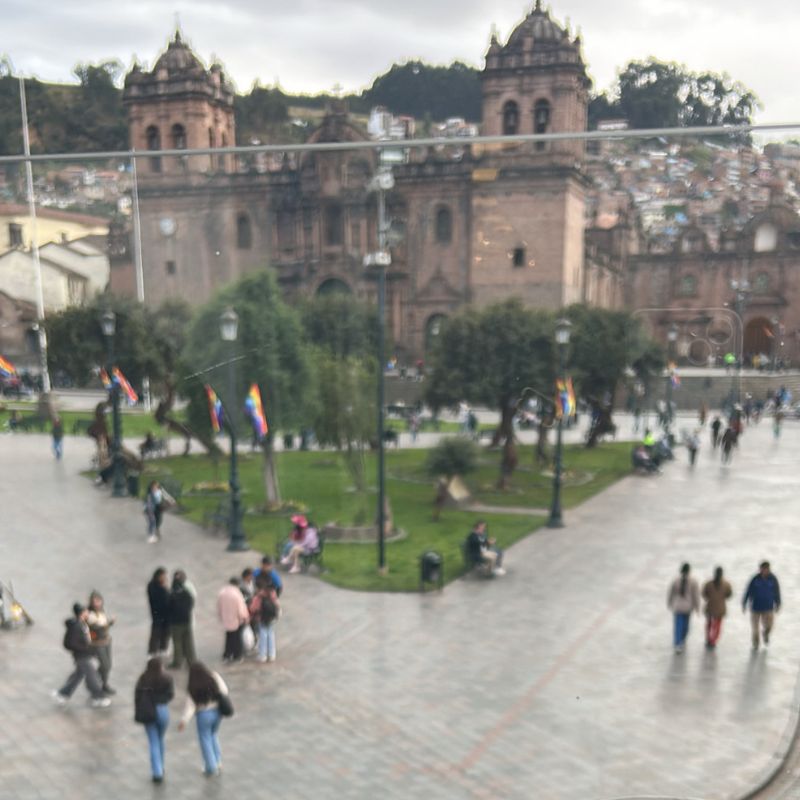 Soft rainy-day view of Cusco’s Plaza de Armas and historic cathedral seen from above through a café window.