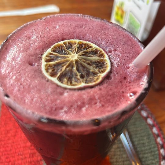 Close-up of a purple fruit juice, chicha morada, topped with a dried citrus slice on a wooden restaurant table in Cusco.