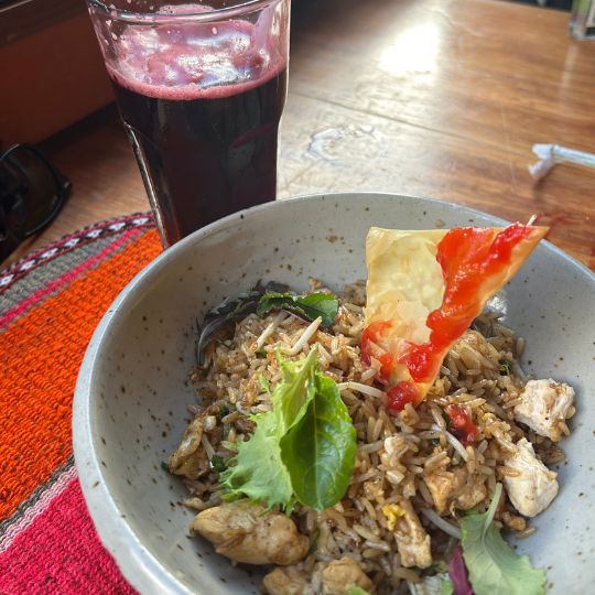 Bowl of Peruvian-style fried rice with vegetables and grilled chicken served with a purple chicha morada drink on a wooden restaurant table in Cusco.