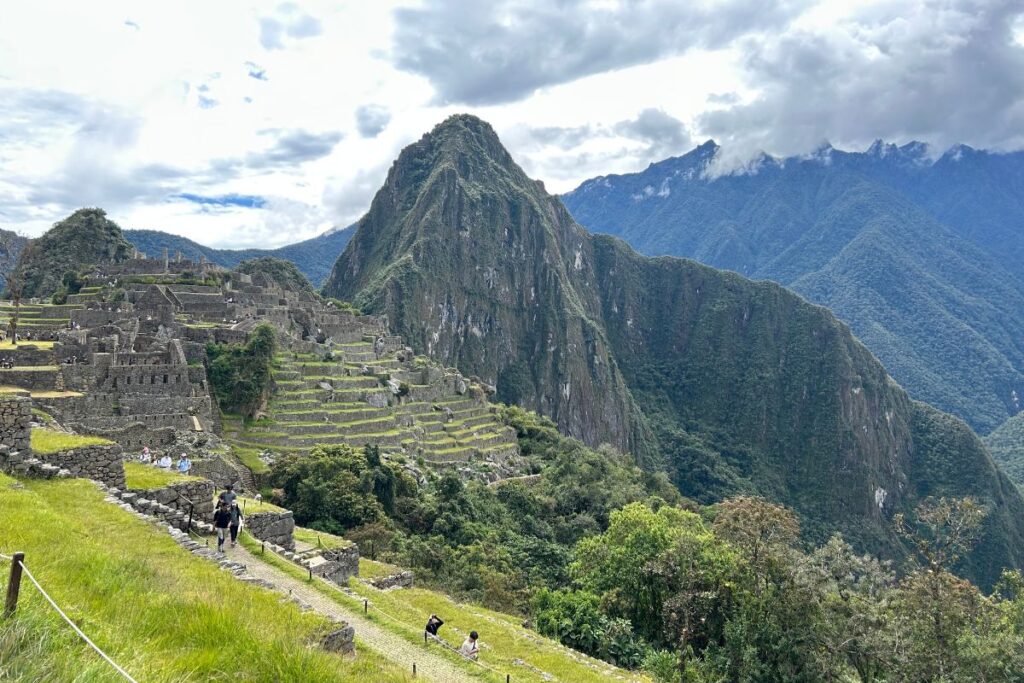 Iconic panoramic view of Machu Picchu with green terraces, stone ruins, and Huayna Picchu mountain rising dramatically in the background.