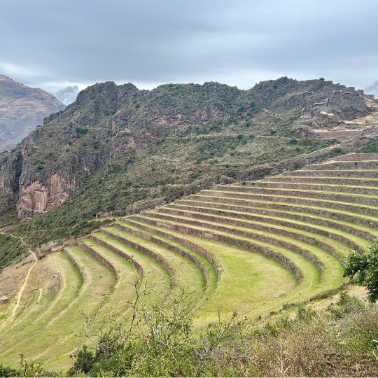 Circular agricultural terraces at Moray surrounded by mountains and cloudy skies in the Sacred Valley.