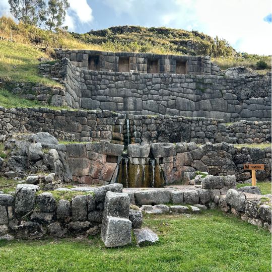 Ancient Inca stone fountain and water channels flowing through finely carved ruins in the Sacred Valley of Peru.