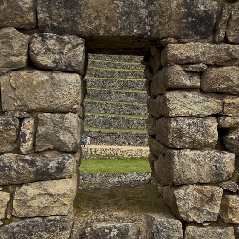 Framed stone doorway at Machu Picchu looking out toward grassy Inca terraces and ancient stone walls.
