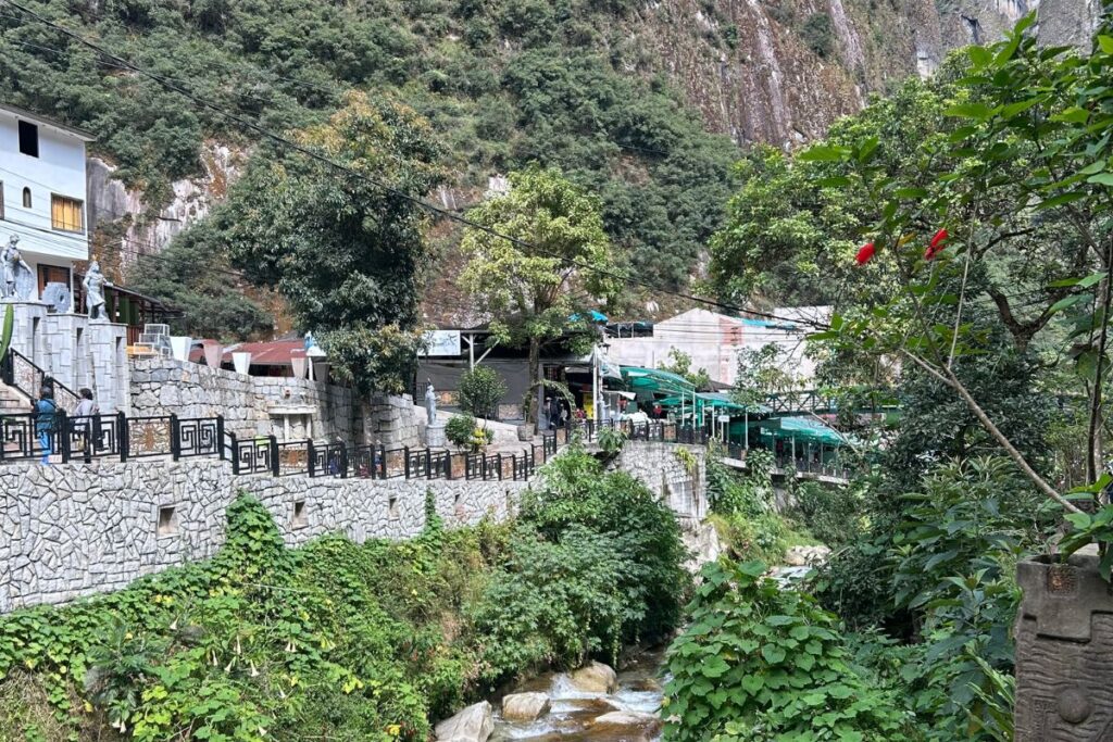 Lush green valley in Peru with a stone walkway and stream running below steep mountainside buildings in Aguas Calientes near Machu Picchu.