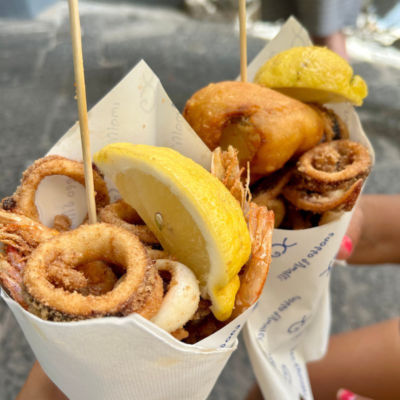 Paper cones filled with fried calamari, shrimp, and seafood, garnished with lemon wedges along the Amalfi Coast.