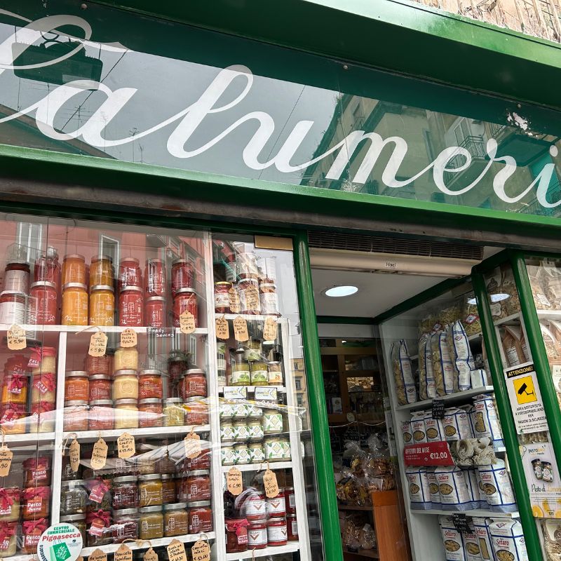 Small specialty food shop in Amalfi displaying jars of sauces, local products, and bags of pasta outside its entrance.