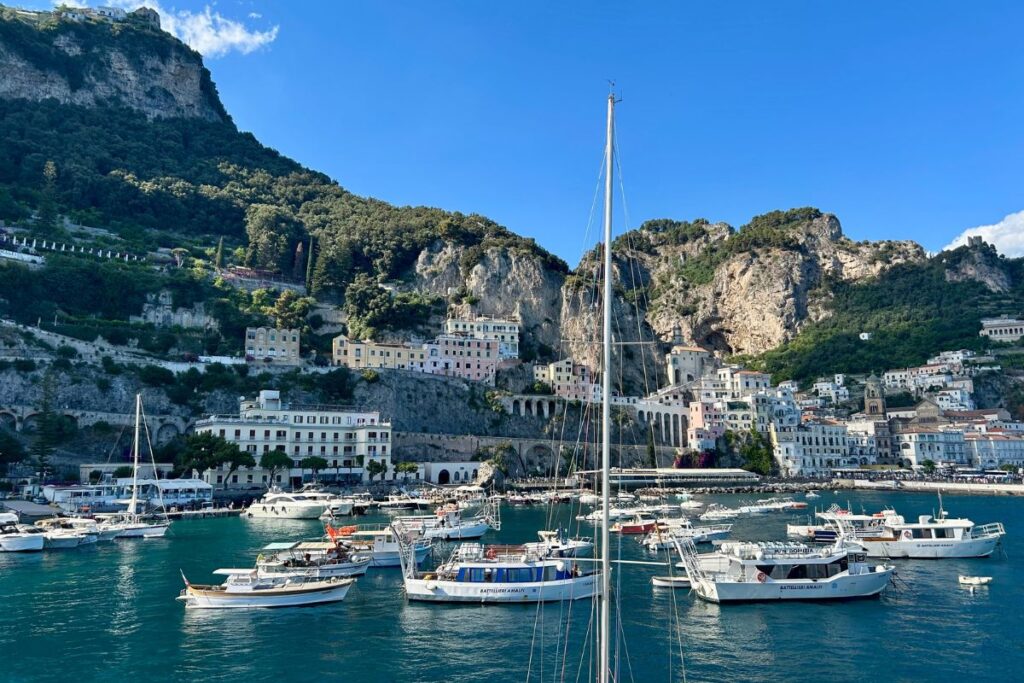 Boats anchored in Amalfi's harbor with colorful cliffside buildings and dramatic coastal scenery surrounding the town.