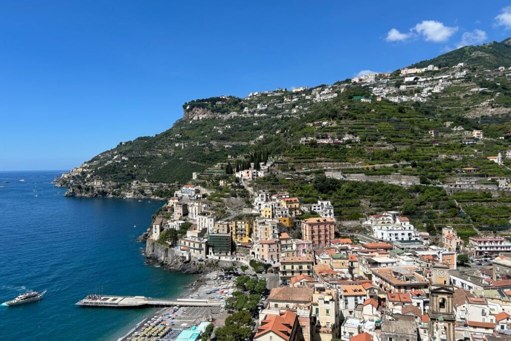 Panoramic view from Ravello overlooking the Amalfi Coast, featuring colorful hillside buildings, terraced mountains, and the Mediterranean Sea below.