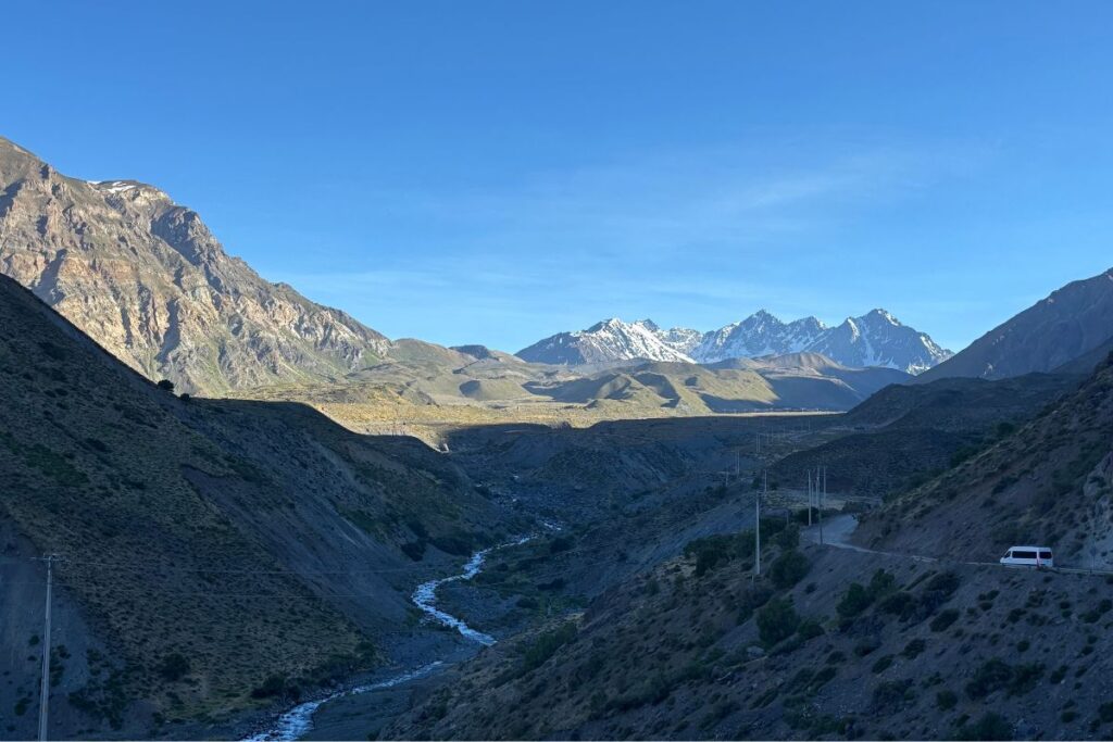Mountain valley in the Andes with a winding river, rugged peaks, and a clear blue sky stretching above the landscape.