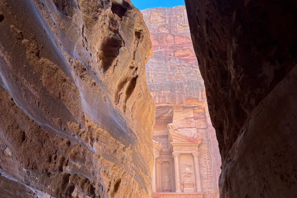 View through the narrow canyon of the Siq revealing the Treasury facade carved into the rose-colored cliffs of Petra.