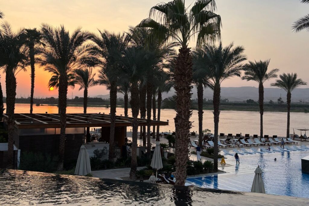 Sunset view over a luxury riverside resort pool, Hilton Luxor Resort, lined with palm trees along the Nile in Luxor.