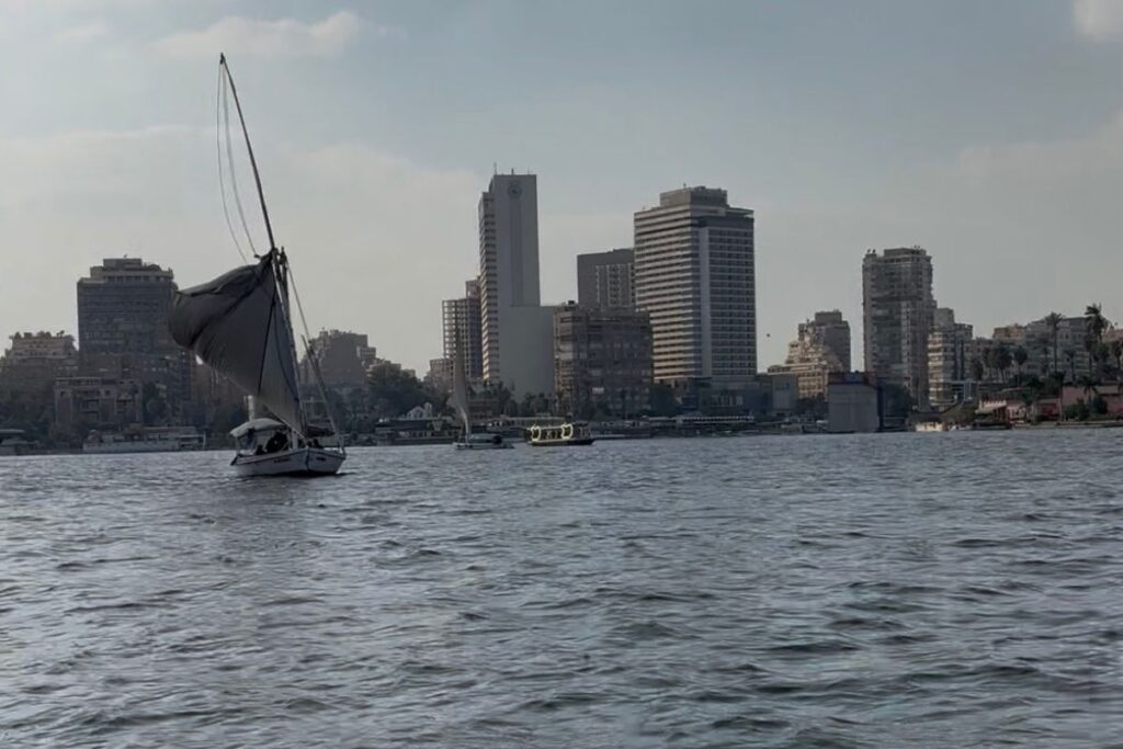 Traditional sailboat floating on the Nile River with the Cairo skyline visible in the background.