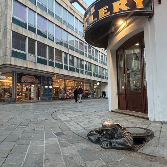 Čumil statue peeking from a manhole cover in Bratislava's Old Town