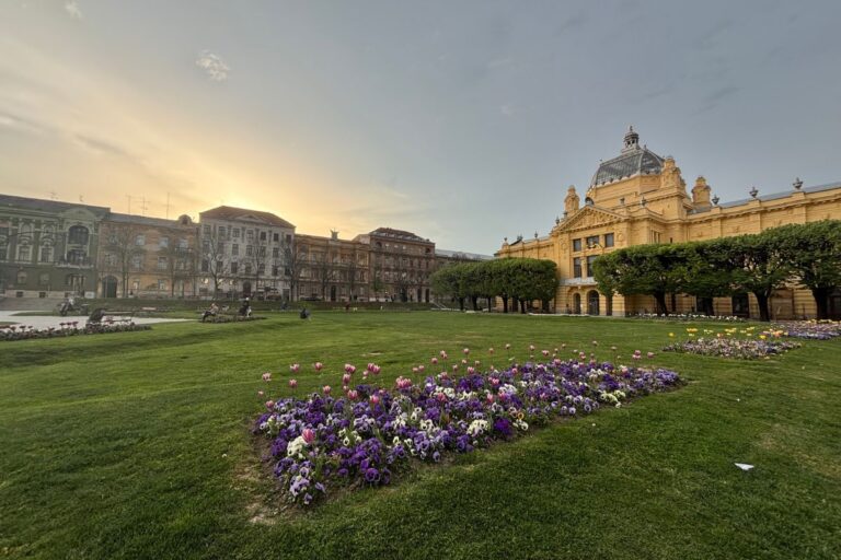 Zagreb Art Pavilion overlooking a green lawn and spring flower beds at sunset