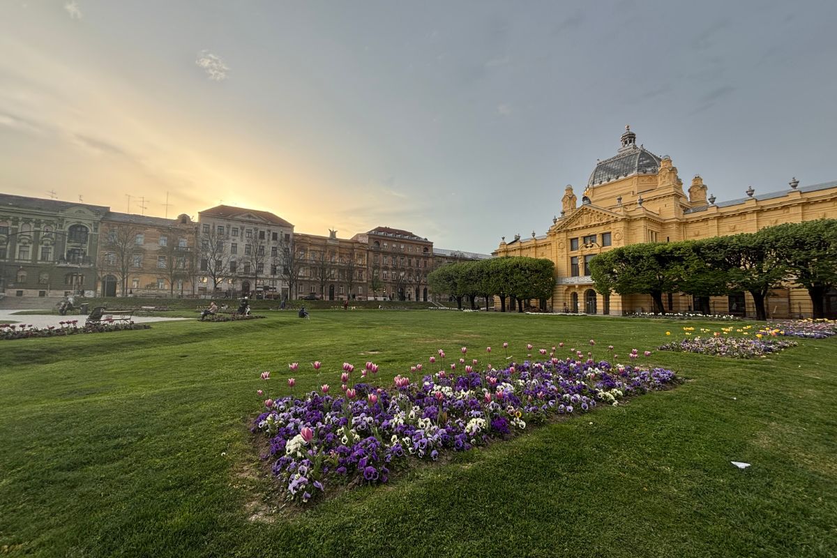 Zagreb Art Pavilion overlooking a green lawn and spring flower beds at sunset