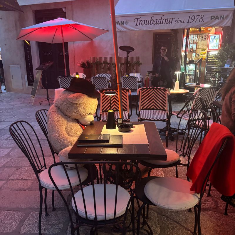 Teddy bear seated at an outdoor café table in Dubrovnik Old Town during the evening