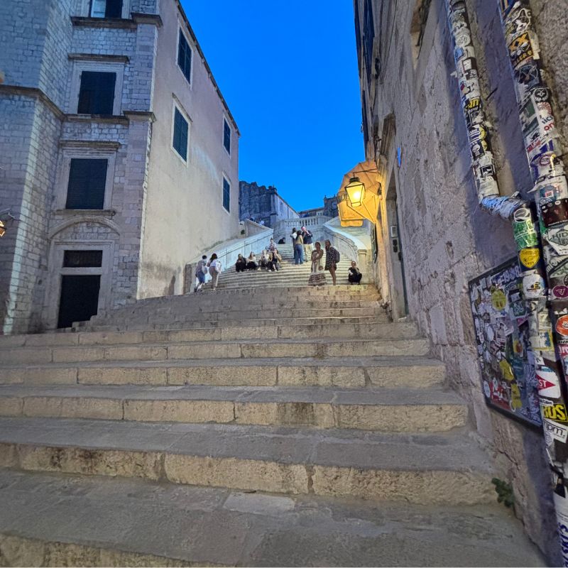 Visitors sitting on the Jesuit Stairs at dusk in Dubrovnik Old Town, Croatia.