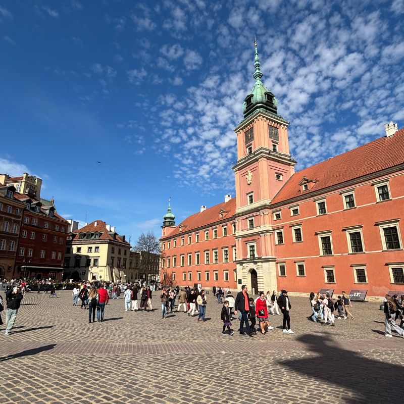 The Royal Castle in Warsaw's Old Town surrounded by visitors on a sunny afternoon.