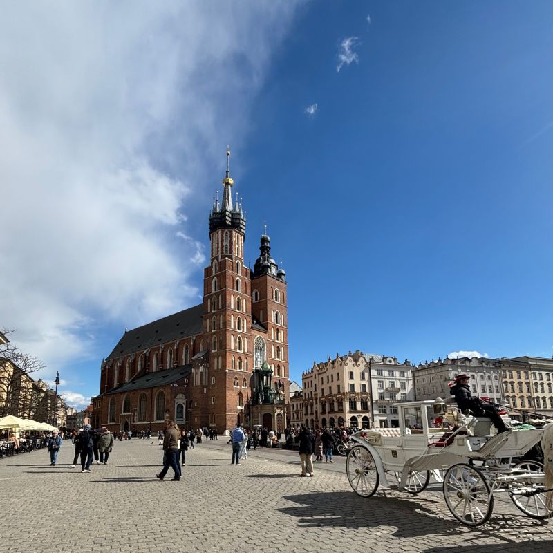 St. Mary's Basilica rising above Kraków's Main Market Square, with a horse-drawn carriage crossing the cobblestone plaza.
