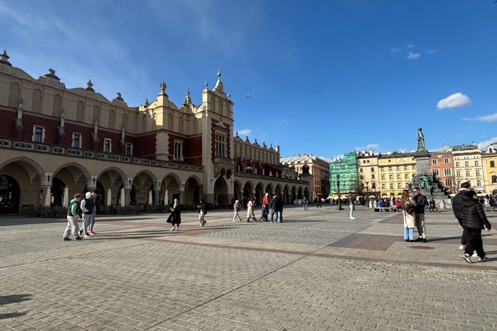 Wide view of Kraków's historic Main Market Square, surrounded by colorful buildings and arcaded townhouses under a clear blue sky.