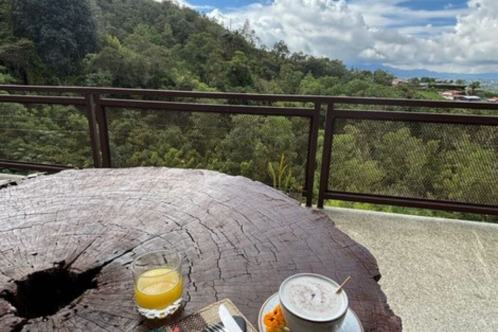 Breakfast with fresh fruit and juice on a rustic wooden table overlooking the forested hills surrounding Cannúa near Guatapé, Colombia.