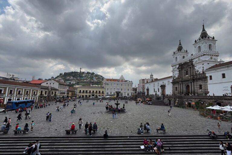 View of Plaza de la Independencia in Quito, Ecuador, with the Metropolitan Cathedral, colonial buildings, and El Panecillo overlooking the historic center beneath dramatic clouds.