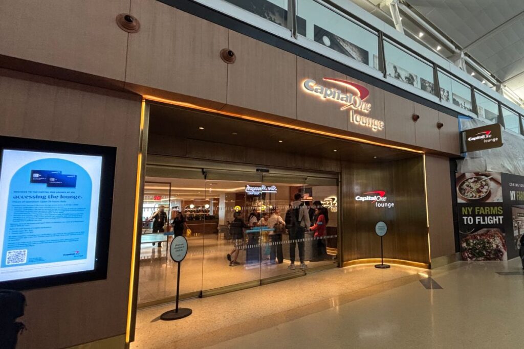 Entrance to the Capital One Lounge at JFK Terminal 4 in New York, featuring the illuminated lounge sign and glass entrance doors.