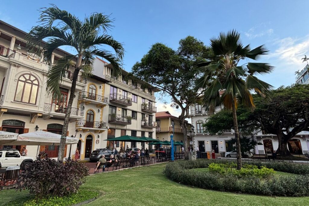 Historic plaza in Casco Viejo, Panama City, with colonial buildings, palm trees, cafés, and landscaped gardens.