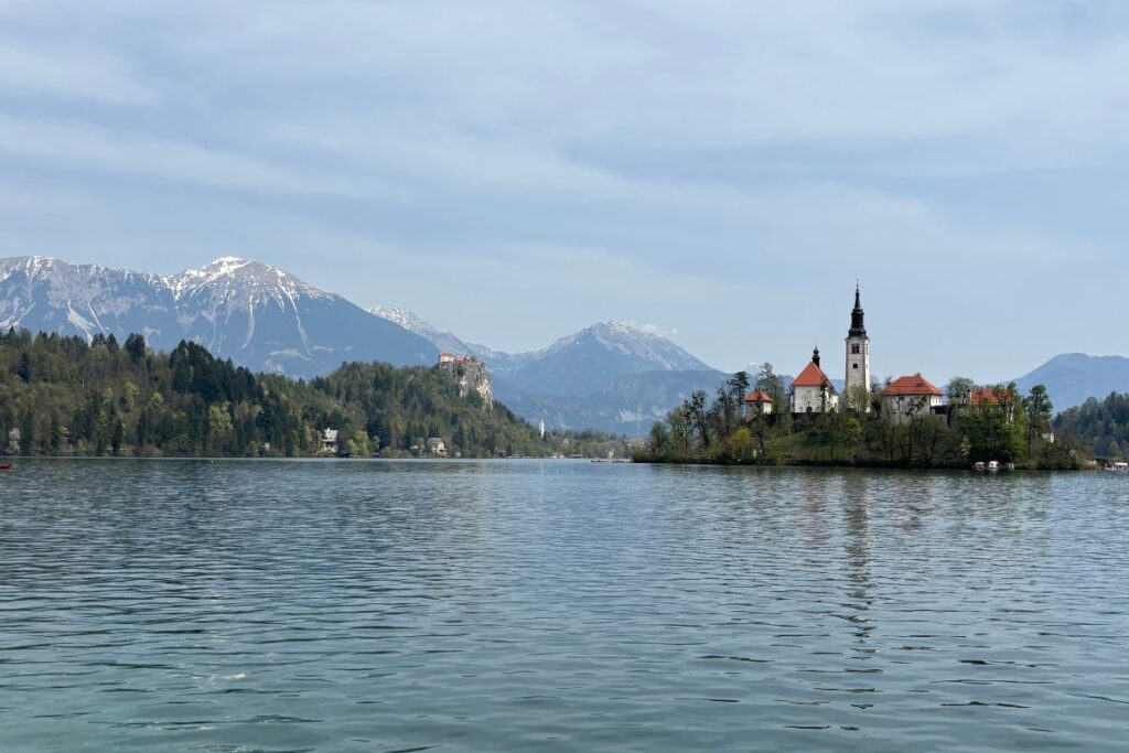 View of Lake Bled in Slovenia with Bled Island, the Church of the Assumption, snow-capped Julian Alps, and Bled Castle in the distance.