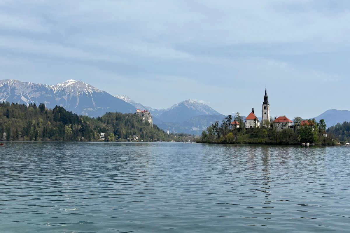 View of Lake Bled in Slovenia with Bled Island, the Church of the Assumption, snow-capped Julian Alps, and Bled Castle in the distance.