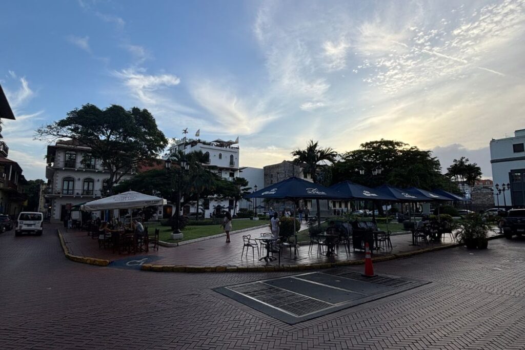 Outdoor cafés and colonial buildings surrounding a leafy plaza in Panama City’s Casco Viejo at sunset.