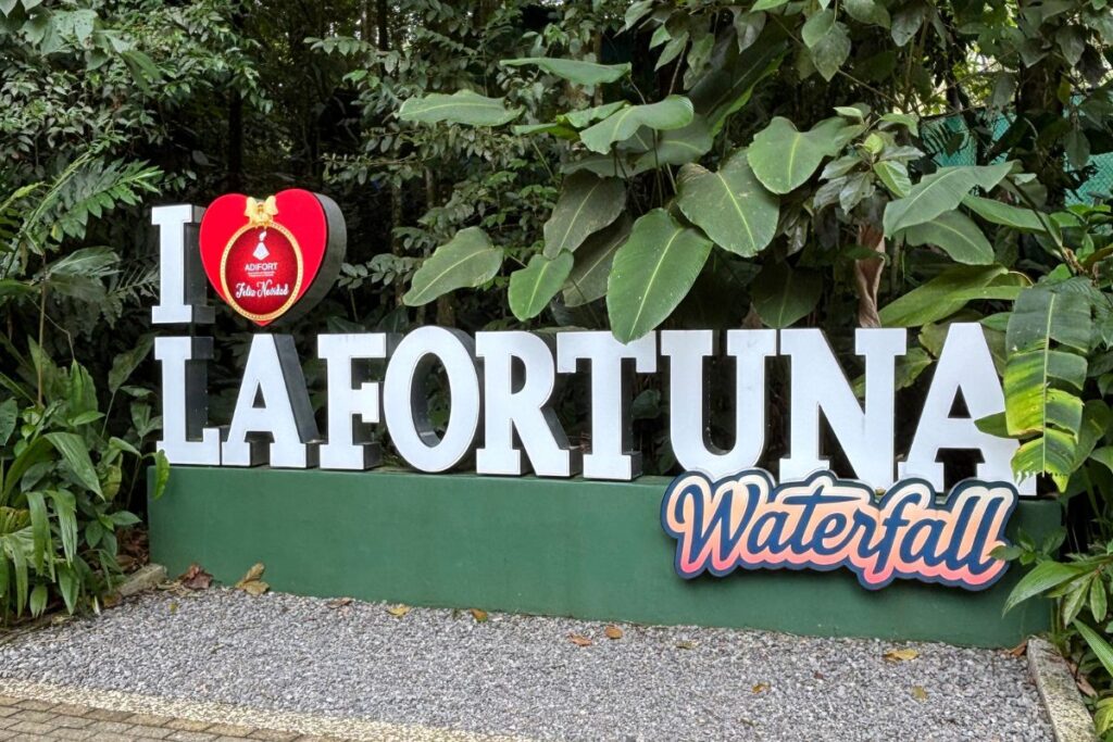 La Fortuna Waterfall entrance sign surrounded by tropical rainforest in Costa Rica.