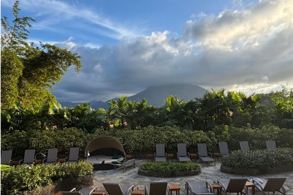Alt Text:
View of Arenal Volcano rising above tropical gardens and lounge chairs at a hot springs resort near La Fortuna, Costa Rica.