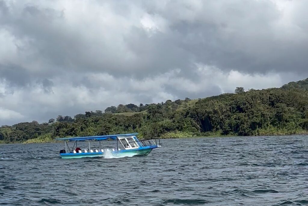 Boat crossing Lake Arenal with rainforest-covered hills in the background, Costa Rica.