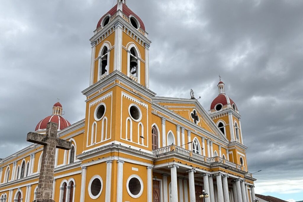 Granada Cathedral with its bright yellow facade and red domes under dramatic storm clouds in Granada, Nicaragua.