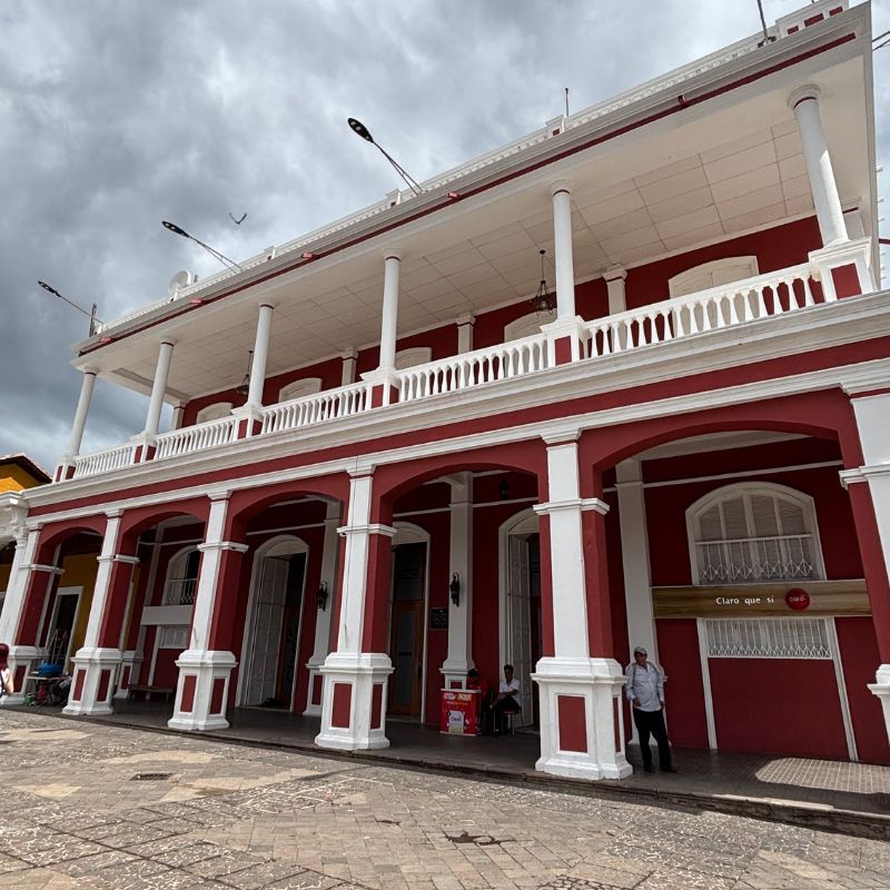 Red colonial building with white columns and balconies along a historic street in Granada, Nicaragua.